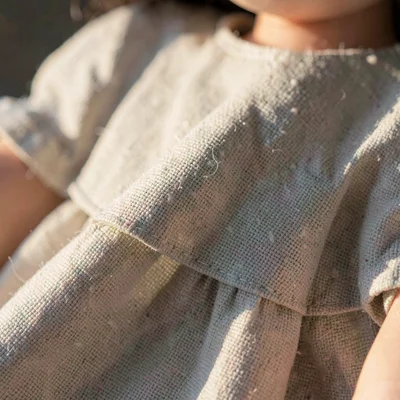 Texture of linen weave on a doll dress with one fold catching warm sidelight