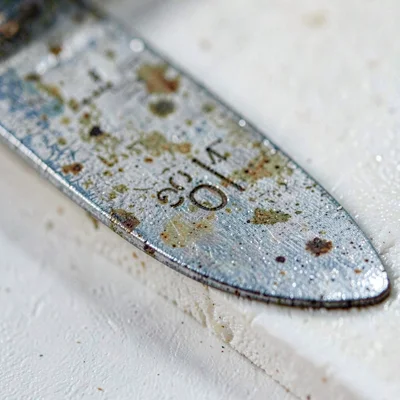Worn-material closeup of a spade edge with use-marks and patina on chalky board