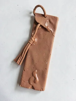 Earnest terracotta bookmark with a slumped tassel and fingernail-pressed corner,