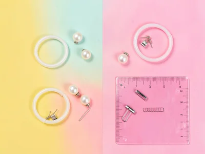 Bird's-eye flat-lay of pearl earrings, plastic bangles, hair clips, and a transl