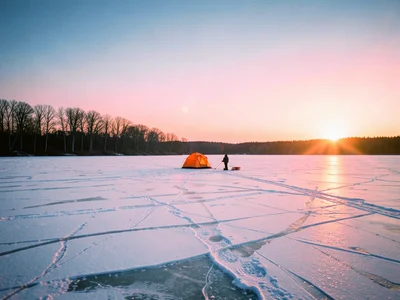 A frozen lake at dawn with a single figure ice fishing, their small shelter tent