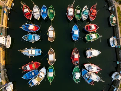 A fishing harbor from above, boats arranged in colorful rows — blue, red, white,
