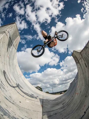 BMX rider upside down in half-pipe, bike and body curved against a warped sky, c