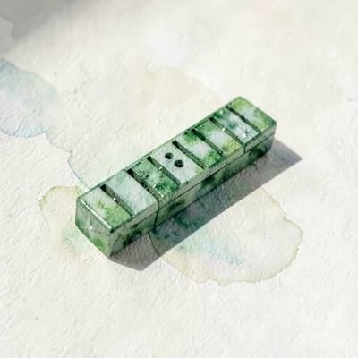 Tiny emerald lowpoly harmonica resting flat with sharp green planes catching tig